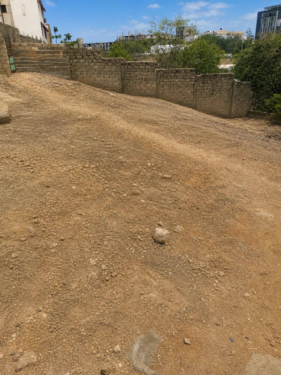 Le terrain vu depuis l'angle nord, mur de clôture et ville au fond